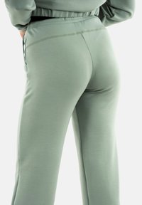 Groene, zachte stof joggers met een gladde textuur, voorzien van een aansluitende taille en rechte benen. Subtiele stiksel details op de taille.