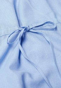Tissu bleu clair avec une couture cousue et un nœud attaché fait de deux bandes de tissu étroites.