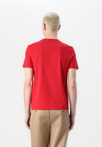 T-shirt rouge à manches courtes avec un col rond, fabriqué en coton lisse, vu de l'arrière avec un design uni et un ourlet droit.