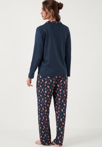 Cămașă de pijama cu mâneci lungi în nuanțe de marină, cu un guler cu model, asociată cu pantaloni cu imprimeu care prezintă turta dulce și ornamente pe un fundal întunecat.