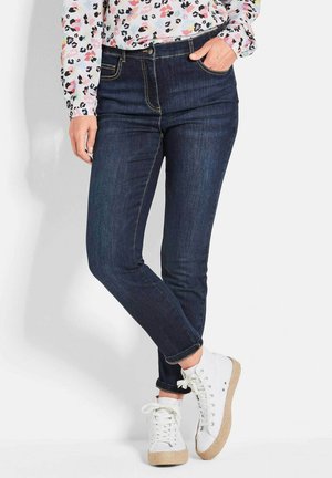 Donkerblauwe denim jeans met een slim fit, voorzakken en omgeslagen manchetten, gecombineerd met witte vetersneakers met een juten zool.