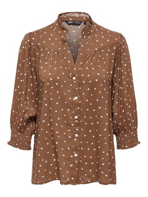 Blouse marron à pois blancs, boutonnée sur le devant, manches 3/4 froncées et col à volants.