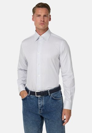 Witte colltrui met blauwe verticale strepen; lange mouwen met knoopmanchetten. Gedragen met blauwe denim jeans en een gevlochten zwarte riem.