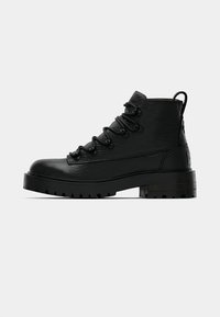 Stivaletti alla caviglia in pelle nera con finitura strutturata, dotati di occhielli metallici e lacci, suola robusta e linguetta posteriore.