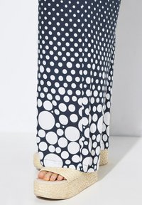 Navyblauwe broek met wijde pijpen en witte stippen, gecombineerd met beige plateau-espadrilles met een geweven textuur.