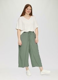 Lichtbeige V-hals T-shirt met korte, brede mouwen; groene, wijde broek met een verstelbare koordtaille; witte sneakers.