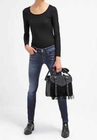 Top negro de manga larga acanalado, jeans azules, bolso negro con detalles de flecos y botas negras hasta el tobillo con suela gruesa.