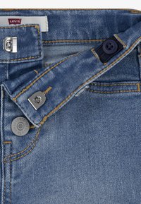 Levi's blå denimjeans med en traditionell knappgylft, kontrasterande sömmar och en silverfärgad metallknapp med logodetalj.