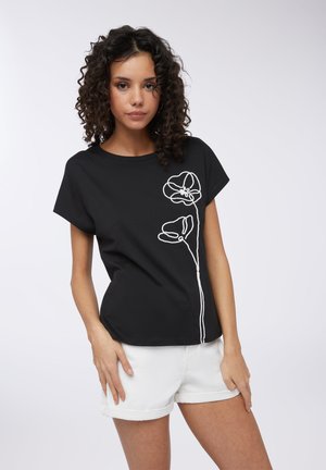 T-shirt nero a maniche corte con design floreale ricamato in bianco sul lato sinistro; abbinato a pantaloni corti bianchi con orlo arrotolato. Tessuto di cotone liscio.