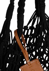 Borsa in macramè nera con manici intrecciati e un'etichetta in pelle marrone, che presenta un design a trama aperta e testurizzata.