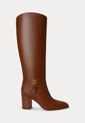 Botte montante en cuir marron avec talon bloc et boucle dorée décorative sur le côté, vue de profil sur fond blanc.