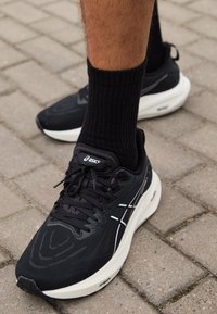 Black athletic shoes with a textured fabric upper, white accents, and signature branding. The sole is thick and cushioned for support.