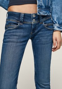 Modré džínové kalhoty slim fit se zapínáním na dva knoflíky, předními kapsami a jemným propracováním na stehnech.