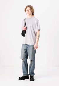Grå kortermet t-skjorte, lyseblå ripped jeans og kraftige svarte sko. Antrekket inkluderer en liten svart skulderveske. Minimalistisk design.