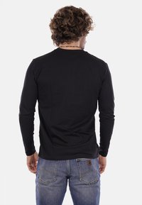 Maglietta nera a maniche lunghe con scollatura rotonda, realizzata in tessuto liscio. Indossata con jeans blu, che mettono in mostra un design semplice e una forma aderente.