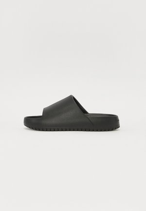 Zwarte schuifsandalen met een gladde, matte afwerking, open teen en een gestructureerde zool met horizontale groeven voor grip.