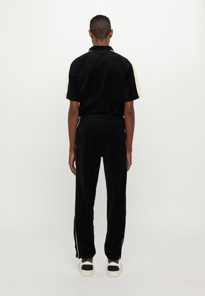 Ensemble de survêtement en velours noir avec un haut à manches courtes et un pantalon à taille élastique, présentant des rayures latérales crème et des baskets blanches.