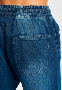Joggers de denim con cintura elástica, en lavado azul oscuro. Presenta un único bolsillo trasero y una textura suave con detalles desgastados.