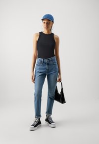 Svart ribbet bodysuit, lyseblå høyhalsede jeans, svarte høye sneakers, og en blå caps; bærende en liten svart veske.