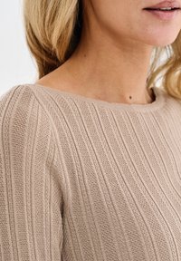 Beżowy sweter z prążkowanego dzianiny z szerokim dekoltem, teksturowanym materiałem i pionowymi paskami, podkreślający lekki i przewiewny design.