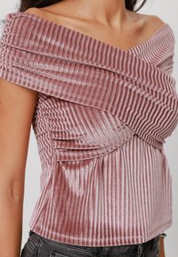 Off-the-shoulder toppi vaaleanpunaisena, valmistettu rakennekankaisesta, ribatusta kankaasta. Edessä on pleatattu yksityiskohta ja se on tiukasti istuva.