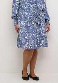 Modra bluzica s potiskom in belimi valovitimi vzorci, v kombinaciji z ujemajočo se večplastno krilom. Črne balerinke dopolnjujejo outfit.