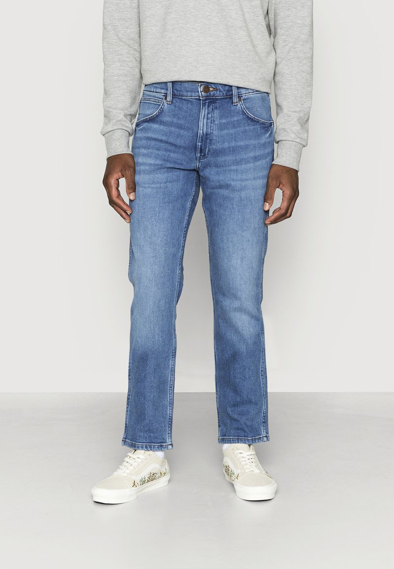 Lichtblauwe denim jeans met een rechte snit, vijf zakken, zichtbare stiksels en een metalen knoop. Draag ze met lichtgekleurde sneakers.