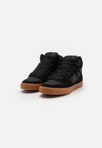 High-top sneakers with black suede and textile upper, rubber gum sole, lace closure, and padded collar for support. Logo detail on side.