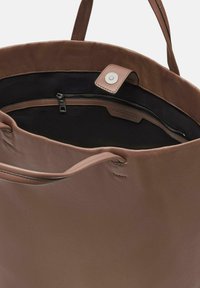 Bruine leren tote bag met een zachte textuur, voorzien van een ritsvak en een vlak ontwerp. Het interieur heeft een contrasterende zwarte voering.