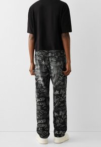 Svart t-shirt kombinerad med grå jeans med graffiti-mönster som har olika vita tryckta designer, stilren form och standardpassform.