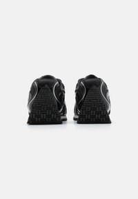 Chaussures de sport noires avec un dessus texturé, un design de talon angulaire et une semelle extérieure en caoutchouc à motifs. Accents réfléchissants le long des côtés.