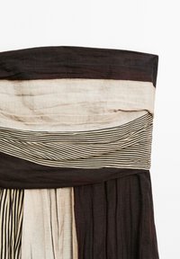 Gestreifter Stoff mit abwechselnden Abschnitten in Beige und dunklen Tönen, plissiert und geschichtet, was ein texturiertes, elegantes Design schafft.
