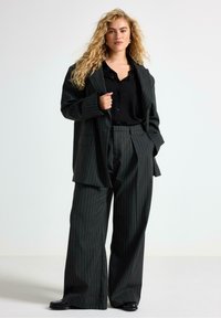Stribet mørkegrøn oversized blazer parret med matchende brede bukser. Sort skjorte med knapper under, glat stof, minimal hardware.