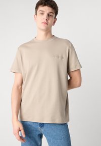 Šviesiai béžinė medvilninė marškinė su apvaliu kaklu ir trumpomis rankovėmis. Ant kairės krūtinės iškilmingai pavaizduotas logotipas "Calvin Klein".