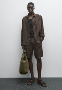 Chemise en lin brun avec des rayures verticales blanches, shorts assortis, débardeur noir, sandales brunes et un sac vert olive. Textures lisses, design décontracté.