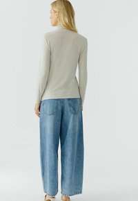Lichtgrijze lange mouw top gecombineerd met losse, lichtblauwe jeans. De stof lijkt zacht met een gladde textuur en zonder zichtbare patronen.