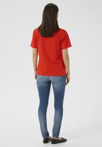 Röd kortärmad skjorta, slätt tyg, rak passform. Bärs med blå slim-fit jeans med bakfickor och ljus tvätt, samt svarta platta skor.