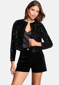 Schwarze Paillettenjacke mit einem cropped Design und rundem Halsausschnitt, kombiniert mit einem schwarzen Satintop und samtigen Shorts. Glatte Textur und glänzende Akzente.