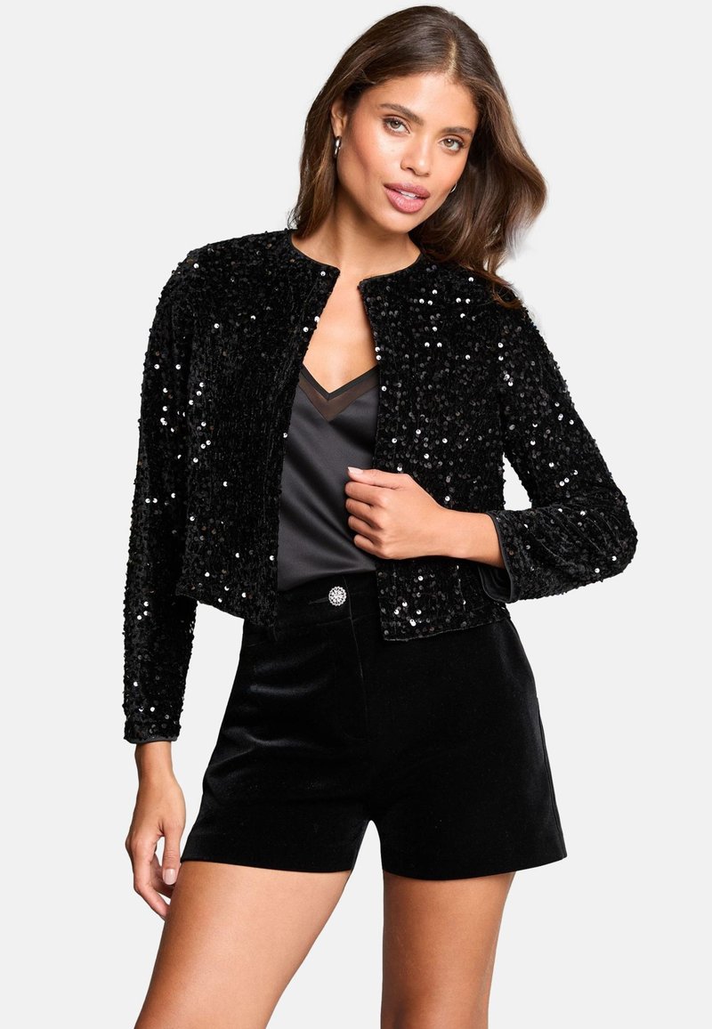 Schwarze Paillettenjacke mit einem cropped Design und rundem Halsausschnitt, kombiniert mit einem schwarzen Satintop und samtigen Shorts. Glatte Textur und glänzende Akzente.