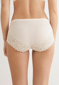 Beige Slips mit Spitzenrücken und floralem Muster entlang der Kanten, aus weichem Material, in mittelhoher Taille und mit glatter Textur.