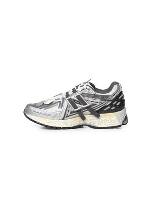 Scarpa da corsa New Balance argento e nera con lacci bianchi e neri, tomaia in mesh e suola spessa e strutturata su sfondo bianco.