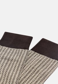 Stickade strumpor med en mörkbrun mudd och ett zigzag-mönster i beige och brunt. Texturen är slät; designen är geometrisk med ett modernt utseende.