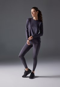 Träningsoutfit bestående av en långärmad mörkgrå topp och åtsittande mörkgrå leggings, tillverkade av ett mjukt och stretchigt material. Svarta sneakers fulländar looken.