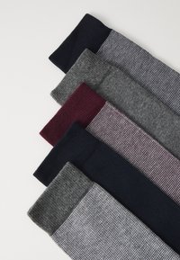 Femm par strumpor arrangerade från topp till botten: marinblå, mörkröd, grå, kolgrå och mönstrad grå. Olika texturer och stickmönster.