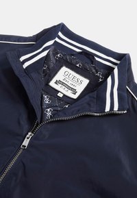 Marine windbreaker jacket met rits en gestreepte gebreide kraag. Voering van binnen heeft een gepatterneerde stof en een merklabel.