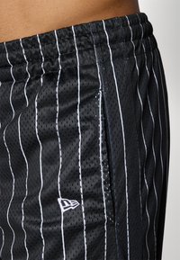Black athletic shorts made from breathable mesh fabric featuring vertical white stripes, an elastic waistband, and a small logo on the side.