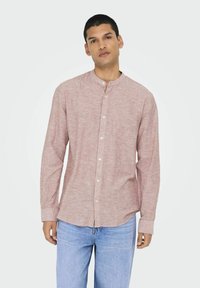 Camicia button-up rosso chiaro con colletto a band, maniche lunghe e stoffa strutturata. Abbinata a jeans in denim blu chiaro.