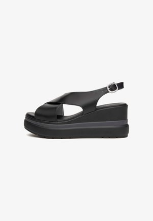 Black wedge sandal with crisscross leather straps, open toe, slingback with silver buckle, and thick textured sole on white background.