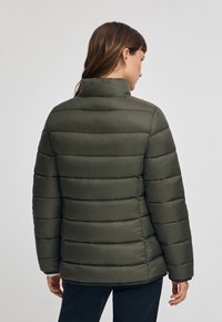 Olivgrön puffjacka med horisontella quiltade sektioner, hög krage och sidofickor. Slätt, lättviktigt tyg med matt yta.