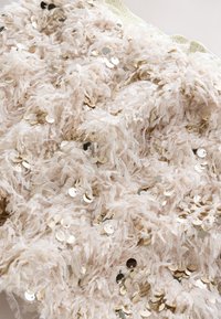 Svijetlobež tkanina s pahuljastom, teksturiranom površinom, ukrašena razbacanim zlatnim šljokicama koje stvaraju vizualni interes i sjaj.